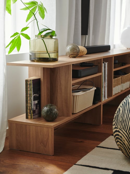In a living room, there is a HOLMERUD side table filled with a cable management box, a vase, a box with lid and decorations.