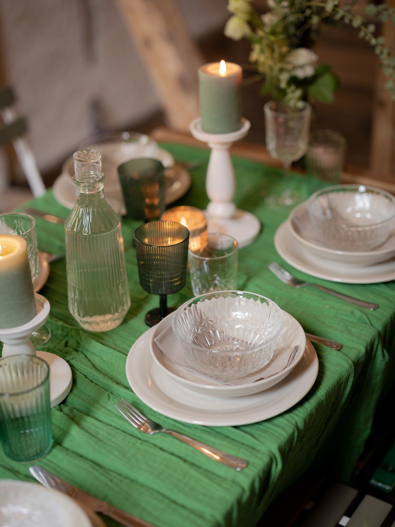 Närbild på en midsommardukning med grön duk, gröna glas och vita tallrikar.