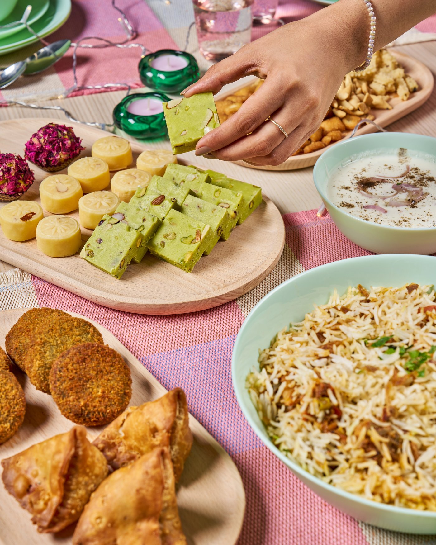 Assorted Indian sweets including barfi and laddoos on a pastel green plate.