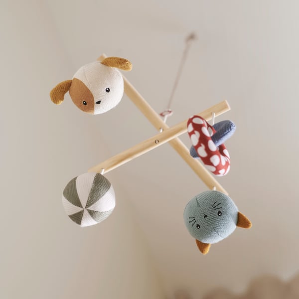 A GULDVÄVARE mobile with four hanging soft toys including a dog, a mushroom and a striped ball, on a wooden cross frame.