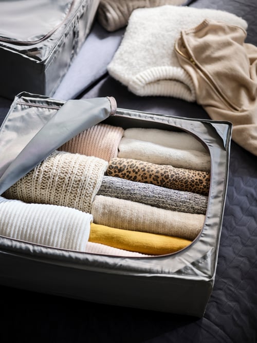 On a textile surface stands a dark grey SKUBB storage case filled with organized, rolled-up garments.