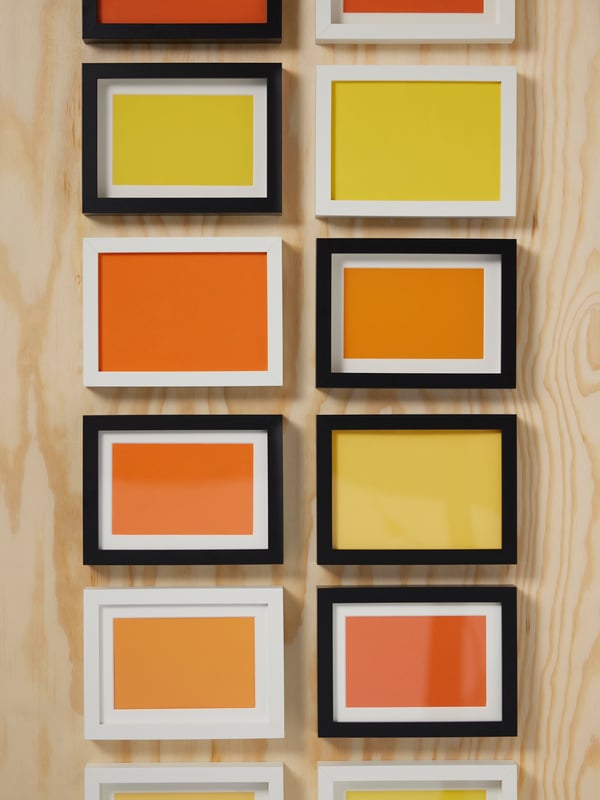 Six black and six white RÖDALM frames mounted in two rows on a wall made from wood.