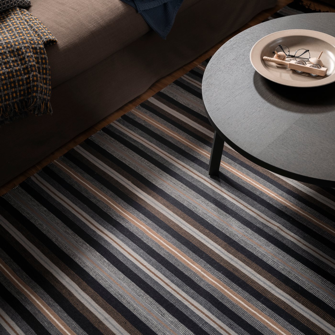 Un bol de service STOCKHOLM 2025 posé sur une table d’appoint STOCKHOLM 2025 sur un tapis RÅVAROR tissé à plat dans un salon.
