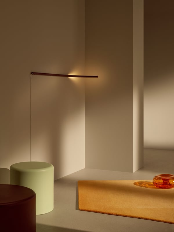 VARMBLIXT linearna zidna lampa postavljena je horizontalno na zidu u minimalističkom prostoru s VARMBLIXT tepihom i stočićima za kafu.