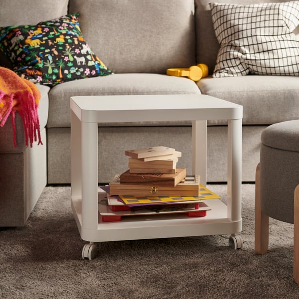 A white TINGBY side table on castors is placed beside a grey sofa, with books and magazines on the lower shelf.