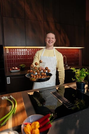 A man is standing in the kitchen with meatballs in a pan