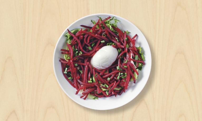 Une salade betterave & œuf poché dans une assiette blanche sur fond bois clair