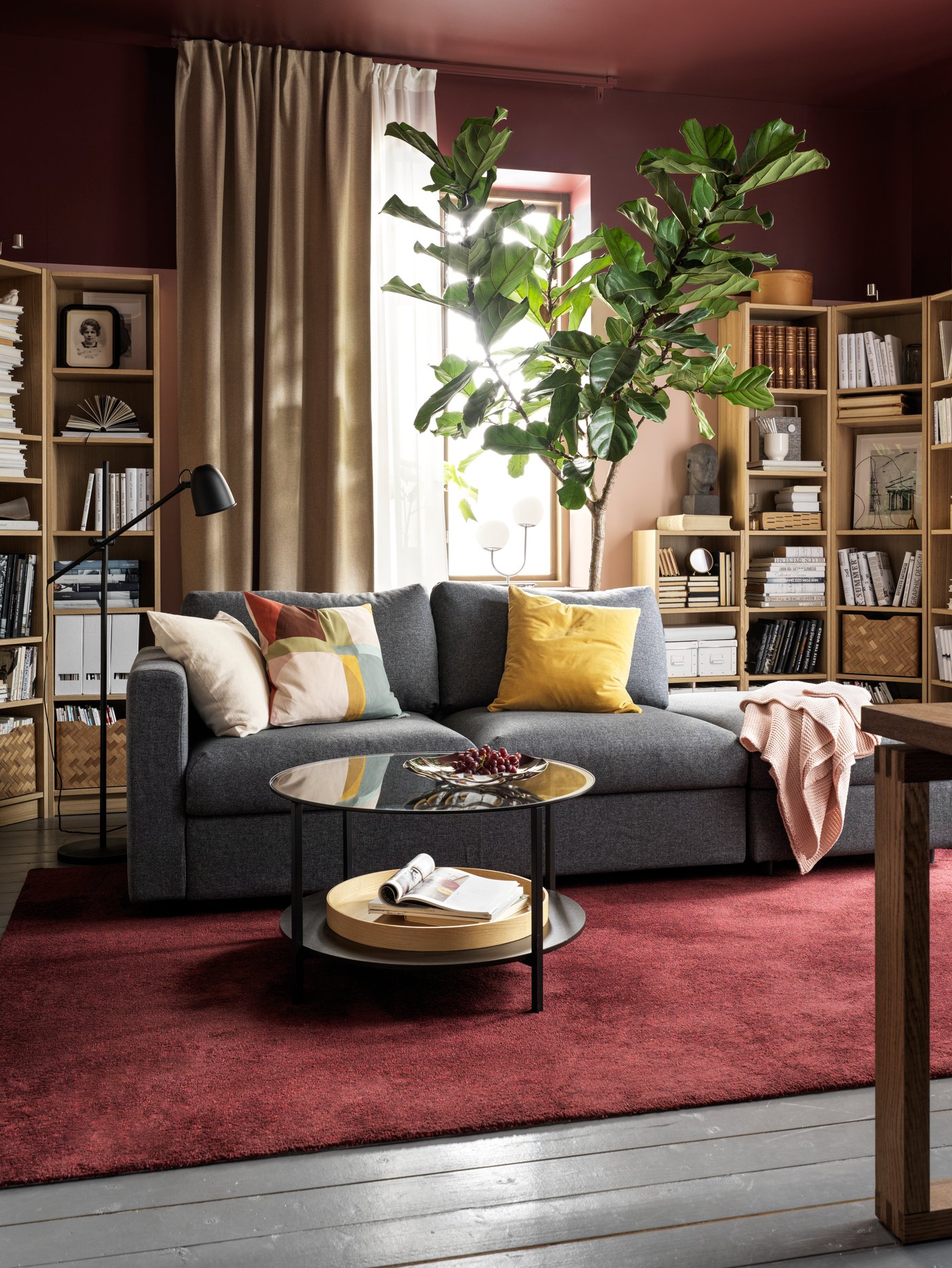 Un living acogedor con grandes libreros en los costados, una planta gigante detrás de un sillón VIMLE y una mesa de centro redonda. 