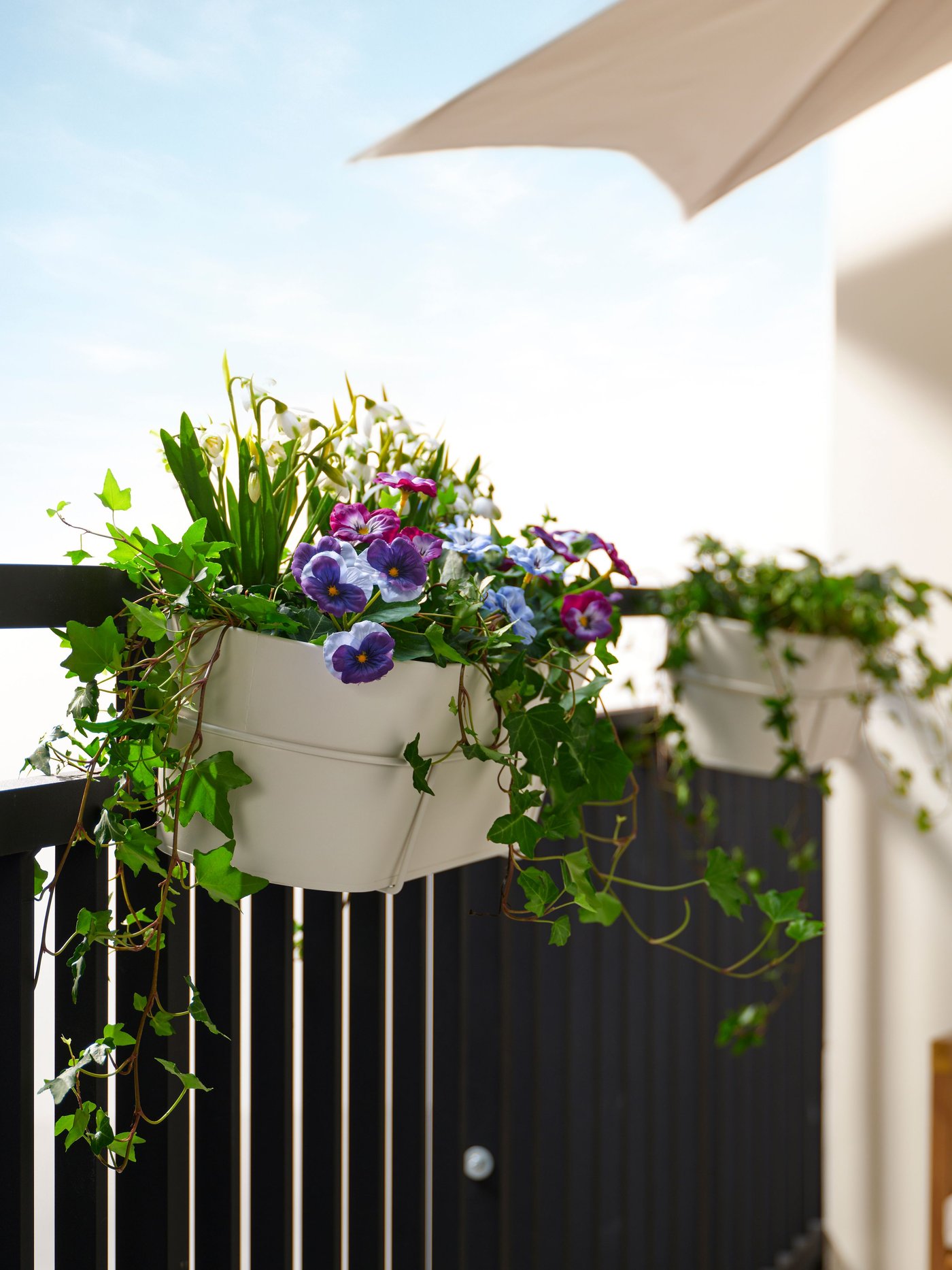 A beige VITLÖK planter with a railing holder, filled with cheerful spring flowers such as pansies. 