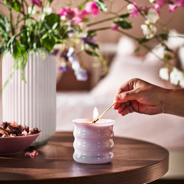 Iemand steekt een lila JÄMNMOD geurkaars aan met een lucifer.