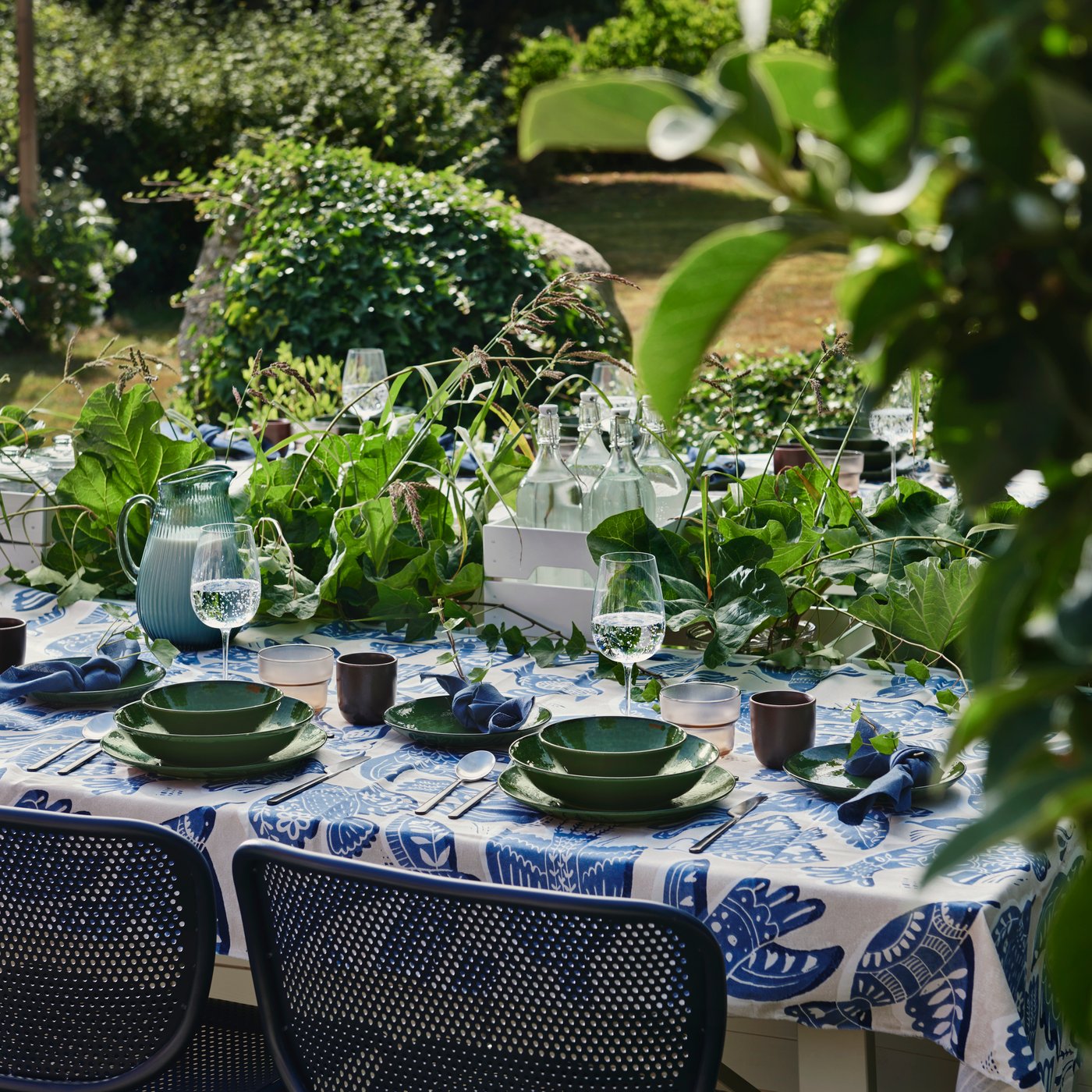 A garden dining area set with a green PELARKAKTUS deep plate on a table layered with foliage and tableware.