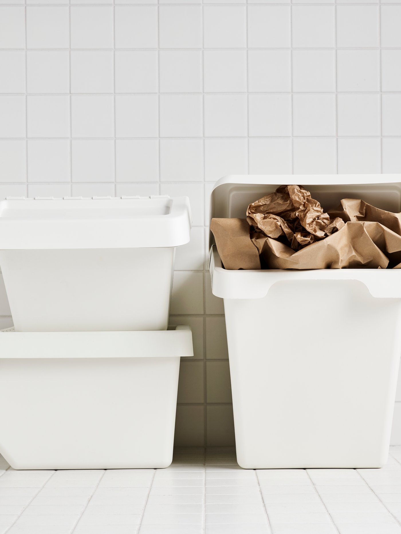 Three white SORTERA waste bins in a white-tiled room.
