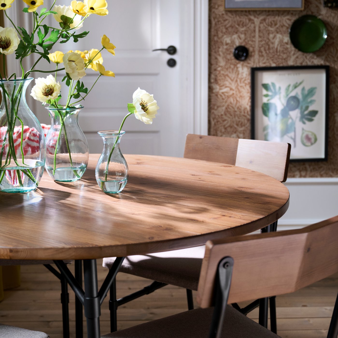 A dining room with GRÖTÅN table in pine/brown stained, styled with glass vases of yellow flowers and wooden chairs.