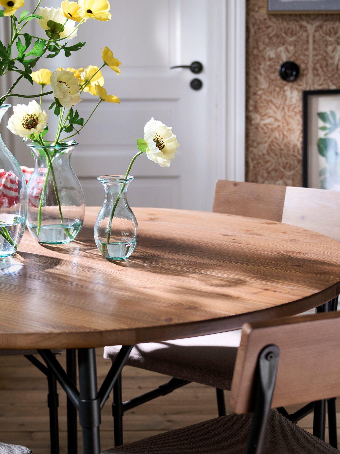 A dining room with GRÖTÅN table in pine/brown stained, styled with glass vases of yellow flowers and wooden chairs.