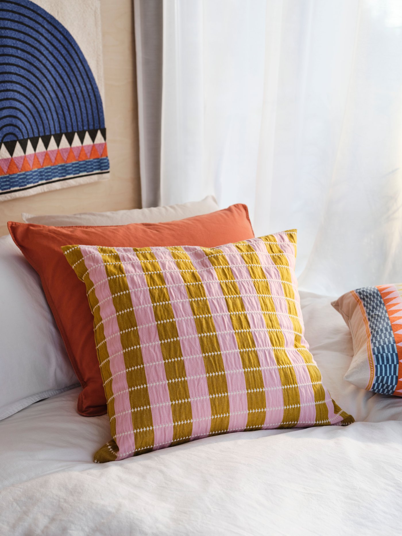 Two cushions, one of them with a pink/beige OMMJÄNGE cushion cover, rest against a larger white cushion in a bed.