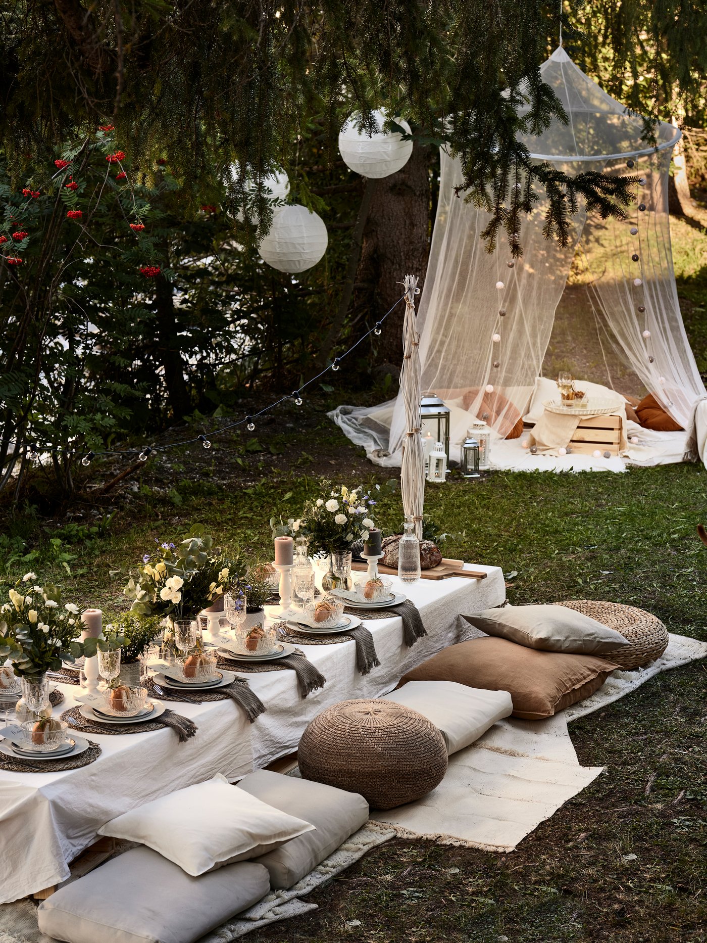 Ett festligt dukat långbord ute i det gröna med kuddar som sittplatser.