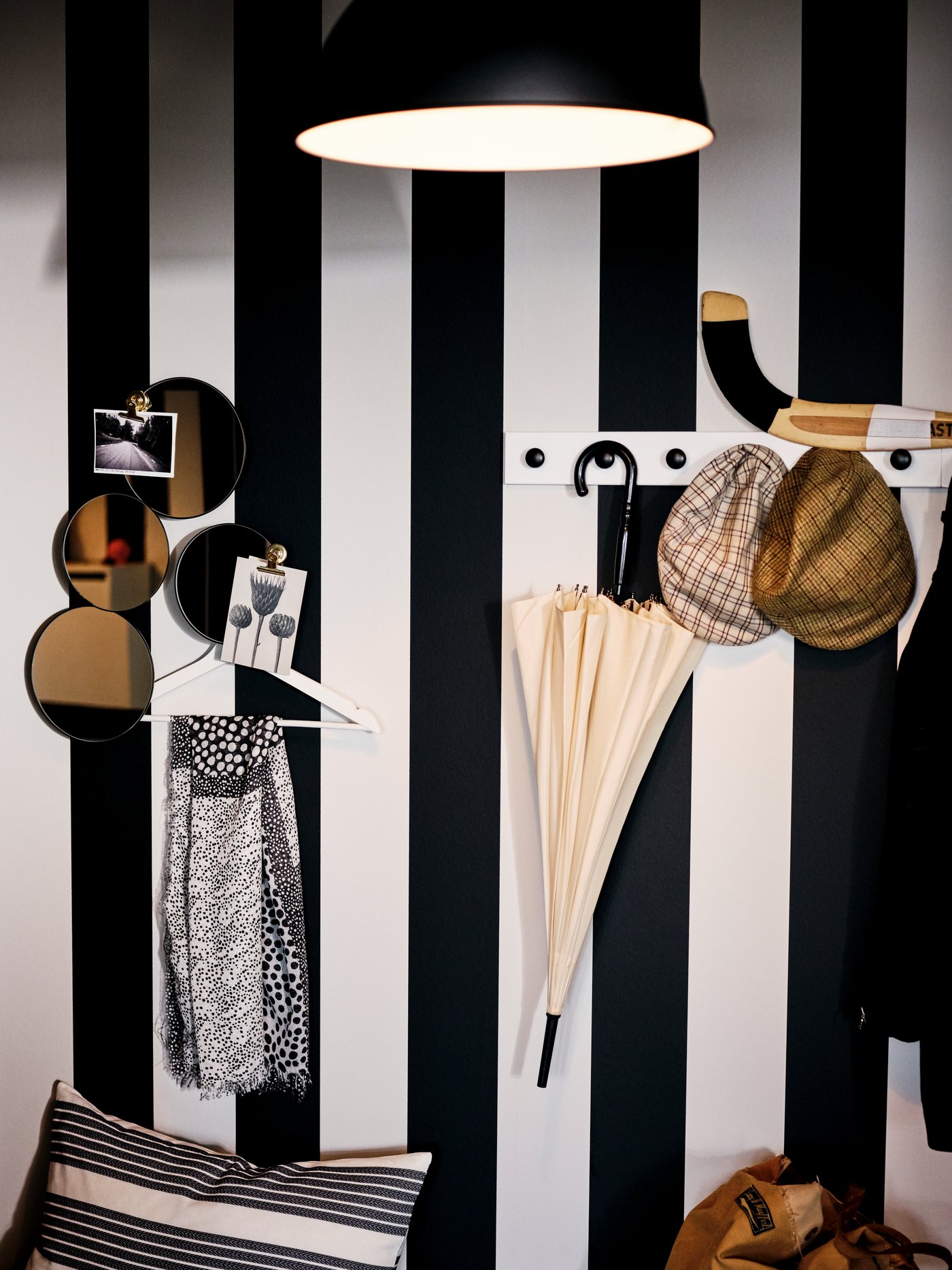 On a broad-striped black-and-white wall hang various items, some from black ENERYDA knobs on a white-stain LURT rack.