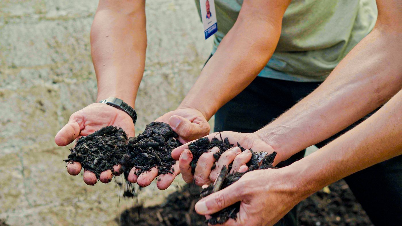 Two individuals extend their arms, each holding handfuls of rich, dark soil.