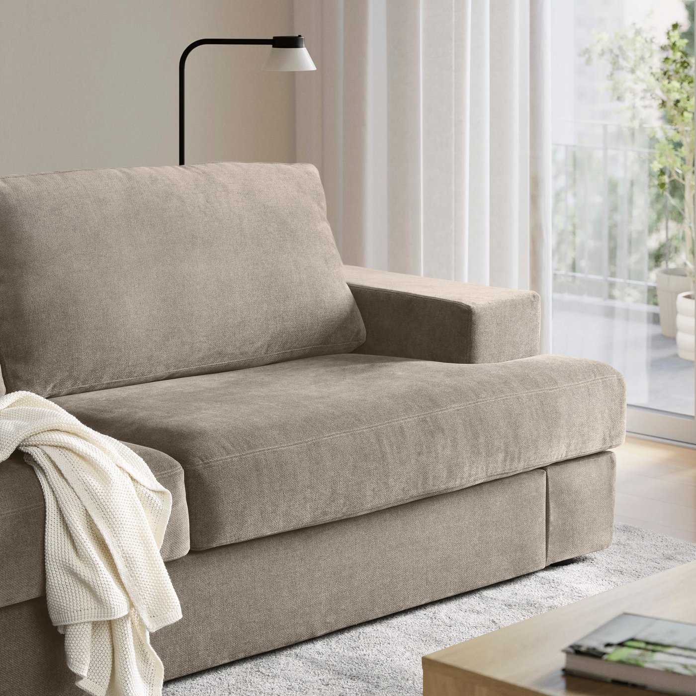 Modern beige loveseat with a draped throw blanket beside a window in a bright living room.