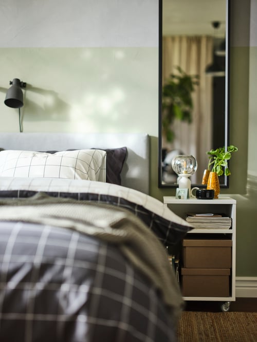Une table de chevet VIHALS blanche près d’un lit matelassé GLADSTAD gris clair recouvert d’une housse de couette VITKLÖVER.