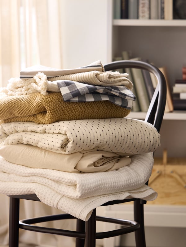 A pile of folded textiles in beige, white and yellow on top of SKOGSBO chair in dark brown.