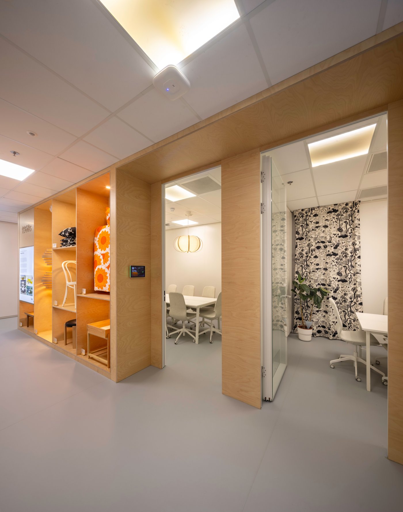 Un couloir de bureau avec trois salles de réunion distinctes, chacune avec son propre intérieur : une alcôve orange, une salle de réunion blanche et un espace vitré avec papier peint botanique.