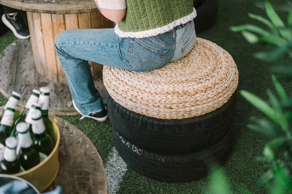 Una donna seduta su un pouf ALSEDA posto sopra due gomme di macchina. Accanto a lei, bevande in un contenitore.