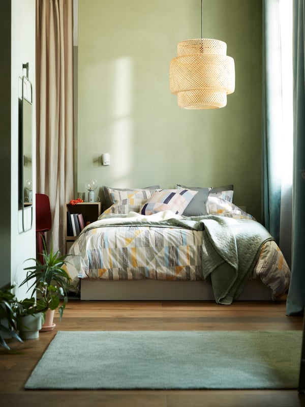 A bedroom with a NYPONLUGGMAL duvet cover and pillowcase set, a SINNERLIG pendant lamp and some EKET cabinets at the sides.