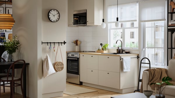 A small, bright kitchen with white walls has beige HAVSTORP fronts and two SUNNEBY cord sets in black textile in the window.