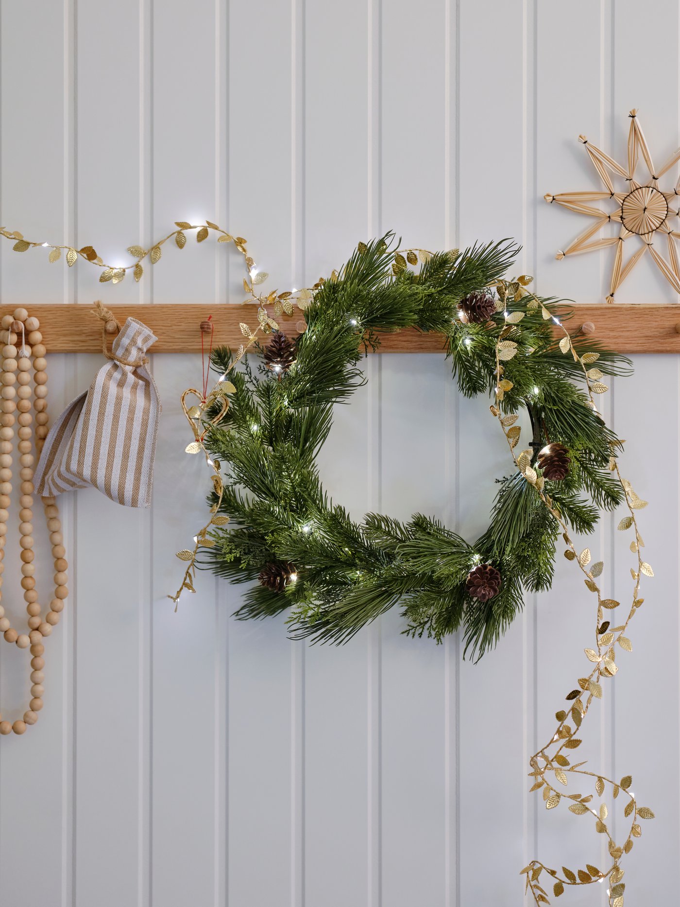 Una corona de navidad colgada en una pared, sobre ella unas guirnaldas LED.