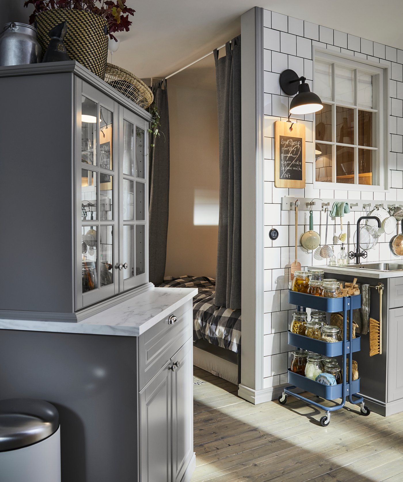 Graue Küchenschränke, RÅSKOG Servierwagen in Dunkelblau und Haken entlang einer weiss gefliesten Wand über einer Spüle