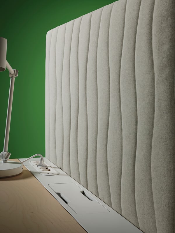 A MITTZON acoustic screen for desk in Gunnared beige placed at the end of a desk, close to a white desk lamp.