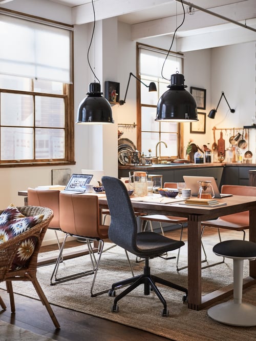 Modern dining area featuring a rectangular table, a conference chair, brown chairs, pendant lamps, and a standing support.