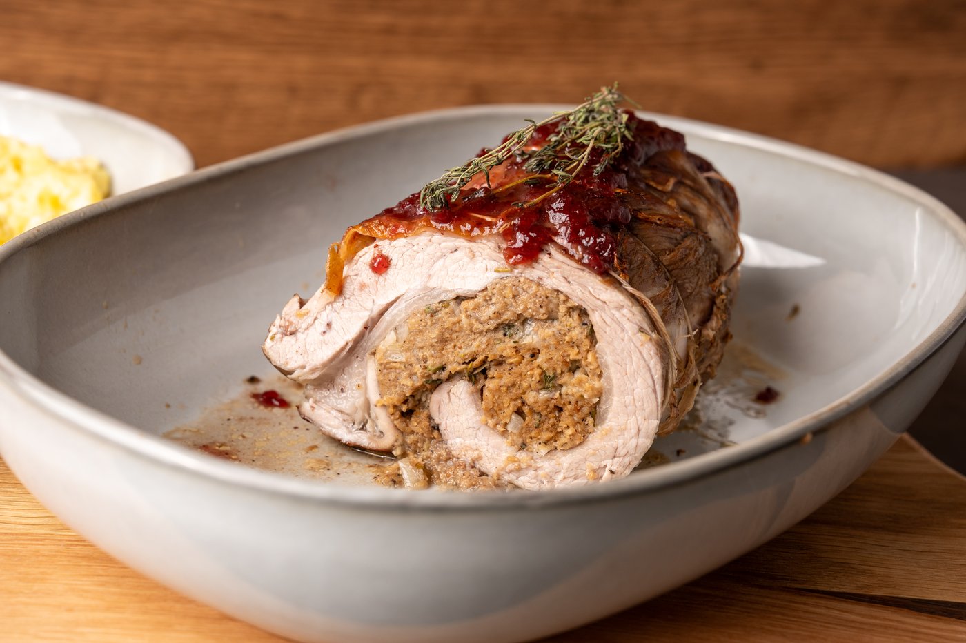 Gerollte Kalbsbrust mit Preiselbeer-Glasur und Kartoffelpüree auf einem weißen Geschirr serviert.