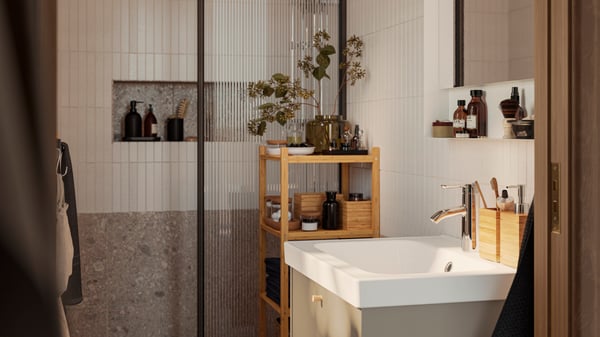 A beige HAVBÄCK wash-stand has a RÅGRUND shelving unit made of bamboo next to it and a mirror placed on the wall.
