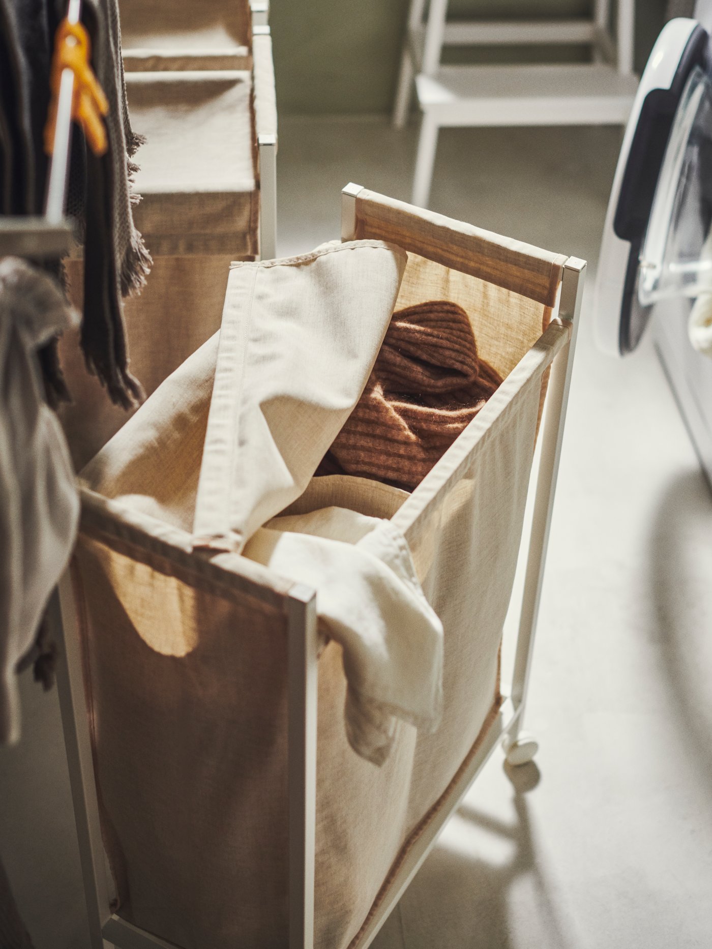 The top of an ENHET laundry bin on castors is open, showing clothes inside. Two more bins are beyond it.