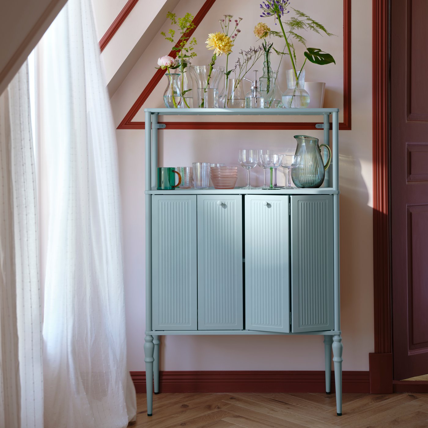 خزانة SÅGMÄSTARE بلون رمادي-أزرق فاتح ومرطبانات زجاجية وأكواب في الأعلى مصفوفة في الداخل بأناقة.