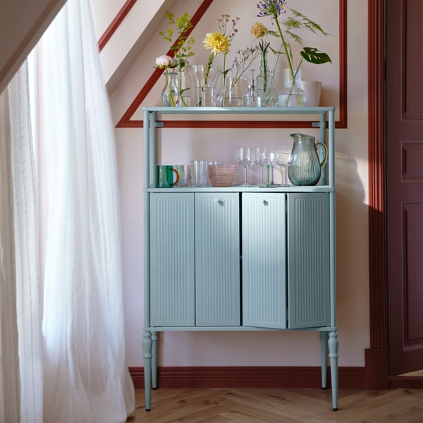 A light grey-blue SÅGMÄSTARE cabinet with glass jars and glasses on top, elegantly placed in a stylish interior.