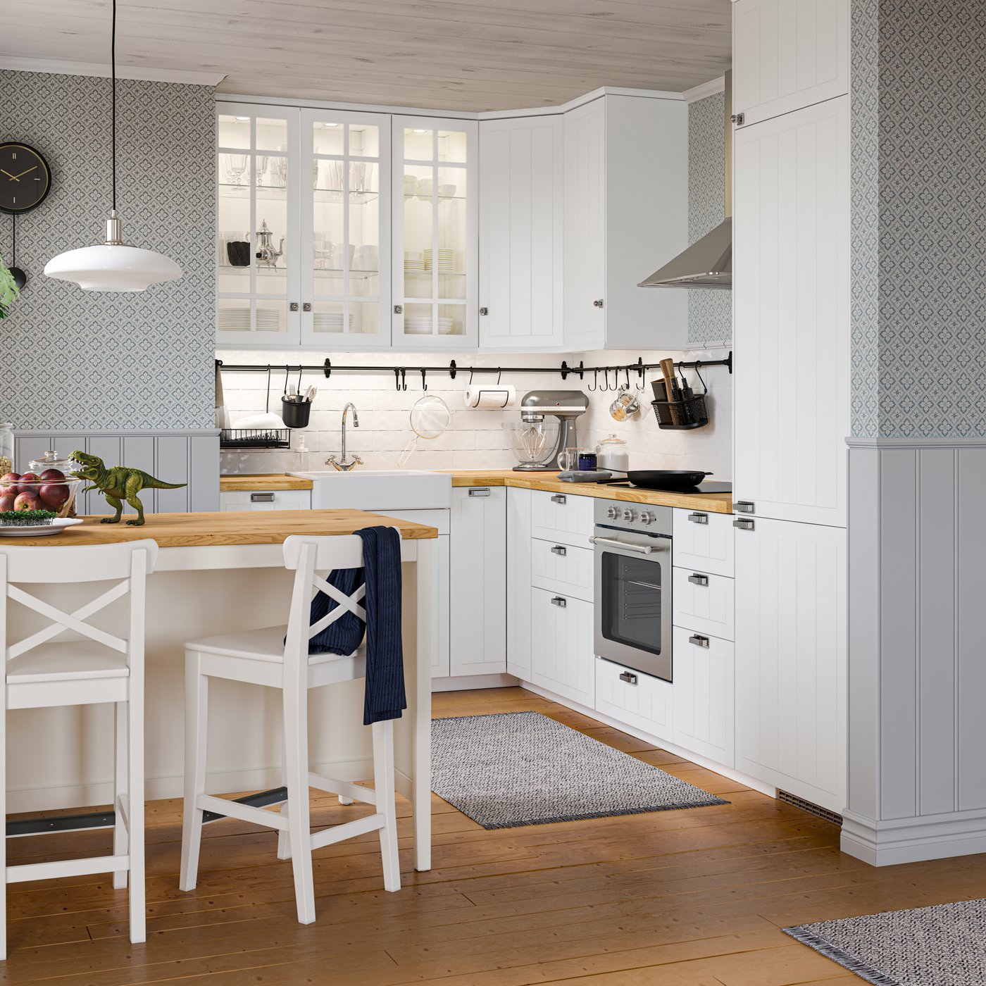 A traditional-style white STENSUND kitchen with wooden floors, floral wallpaper, and a kitchen island and two bar stools.