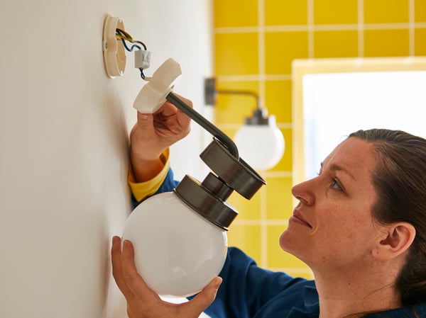Gros plan d'une femme montant une applique sur un mur.