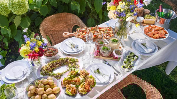 Zu sehen ist ein Tisch im Freien, der mit vielen Leckereien zu Midsommar eingedeckt ist.