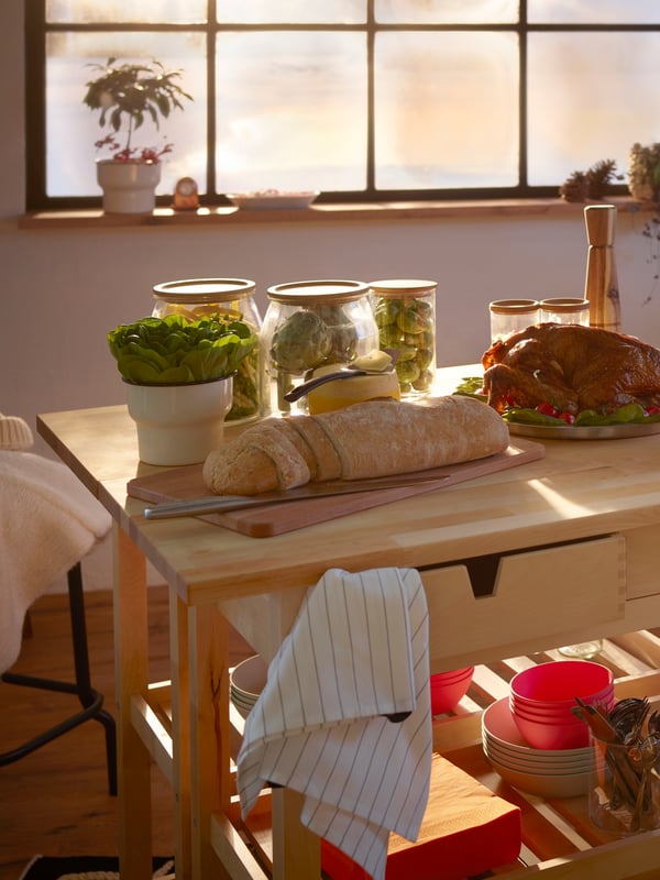 A small wooden kitchen island is set with breakfast foods and stores tableware on the shelves below.