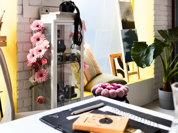 A vibrant home workspace with a BAGGEBO cabinet with glass doors customised with SMYCKA artificial flowers.