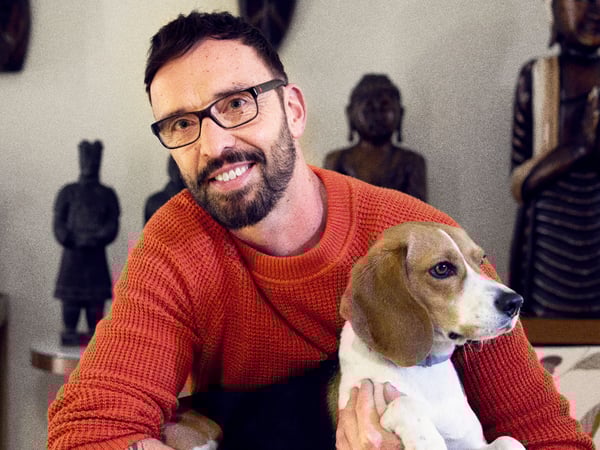 Daniel in his home holding his pet Beagle, a collection of statues in the background.