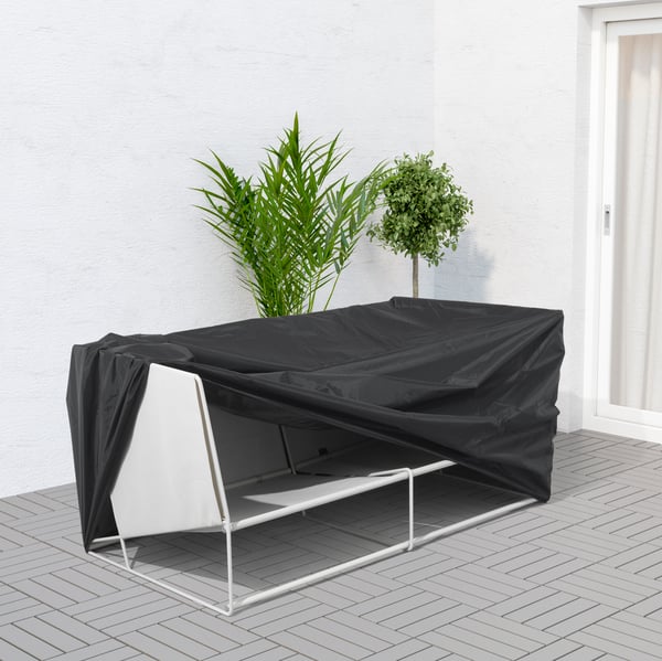 Vit loungesoffa täckt av ett svart möblelskydd utomhus. 