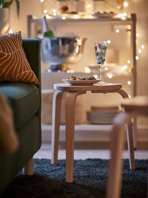 Une assiette et un verre sur un tabouret en bouleau dans un salon festif avec une guirlande lumineuse et un bol à champagne.
