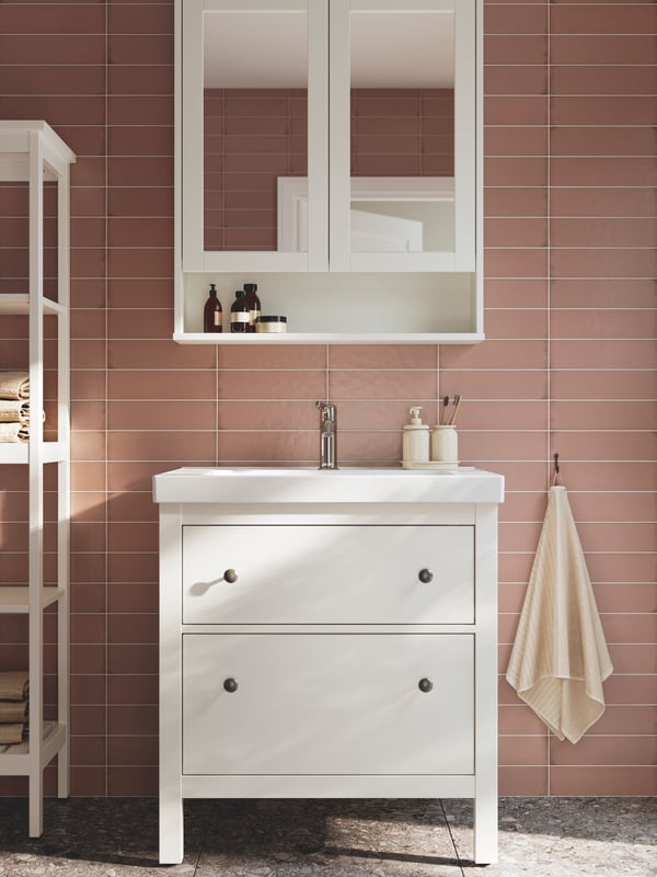 Un baño alicatado de color rosa con un mueble de lavabo abierto HEMNES blanco con dos cajones, un armario con espejo y una unidad de estantería blanca.