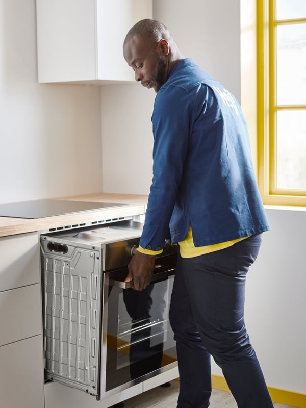 A professional IKEA installer is installing an oven in an IKEA kitchen.