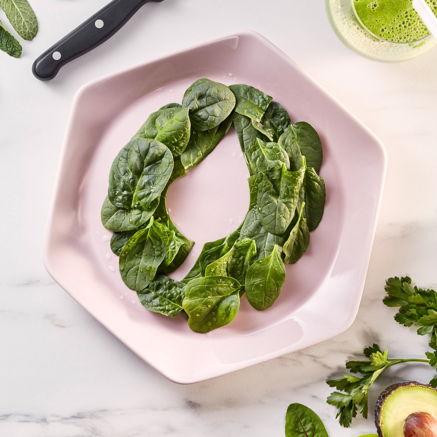 A pink hexagonal plate on white marble worktop. On the plate are baby spinach leaves decoratively arranged in a ring.
