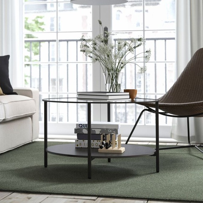 A black round VITTSJÖ coffee table in the living room on a green rug.